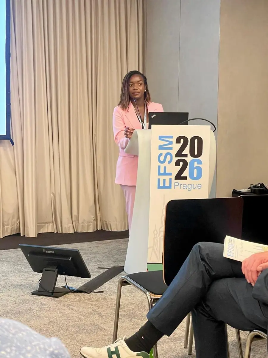 Dr Christine Nyabuto, in a pale pink suit, speaks at a lectern marked EFSM 2026 Prague while audience members look on.