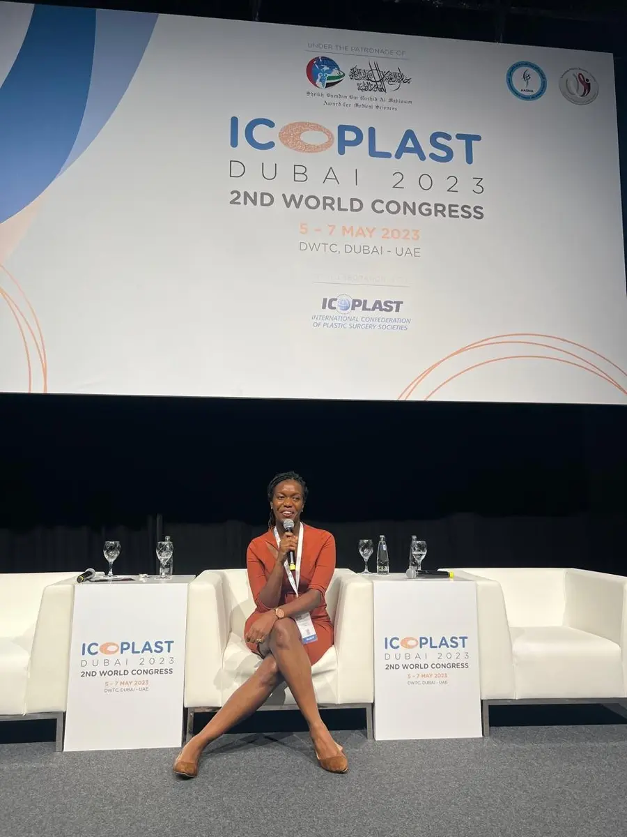 Dr Christine Nyabuto, wearing a rust-coloured dress, speaks into a microphone on stage beneath the ICOPLAST Dubai 2023 2nd World Congress banner.
