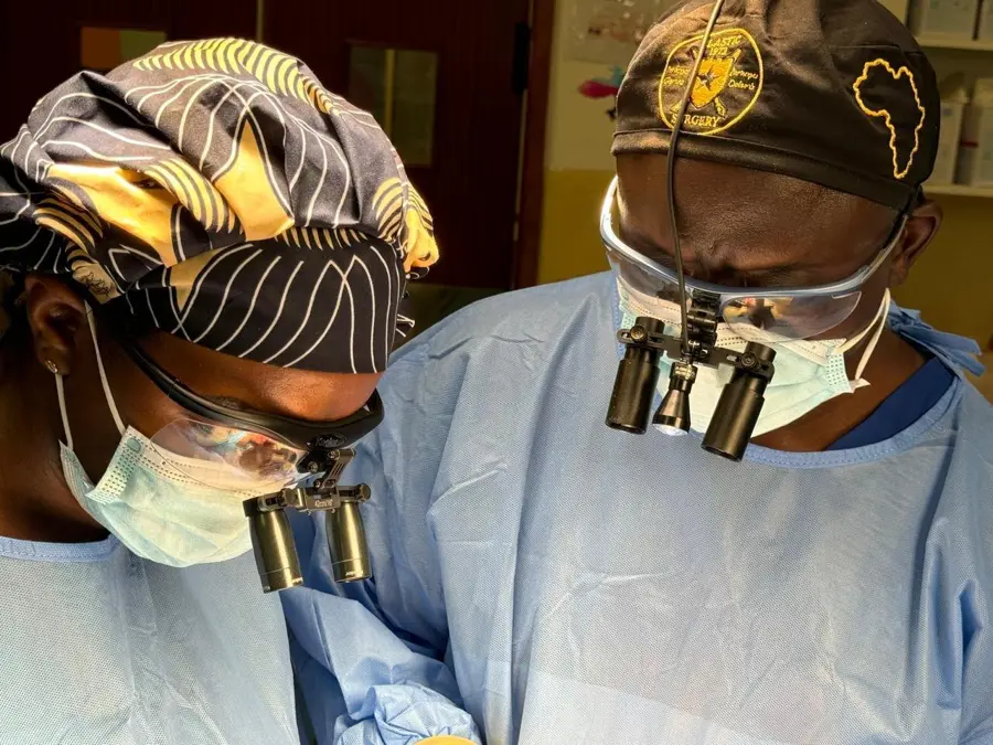 Dr Christine Nyabuto and a colleague in surgical gowns, caps and masks, looking down through magnifying surgical loupes.